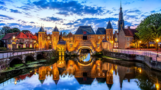 Breedbeeldfoto van de iconische Koppelpoort in Amersfoort, Nederland, met historische stadsmuren en sfeervolle verlichting aan het water tijdens zonsondergang – professionele 8K landmarkfoto voor meubels herstofferen en meubelstoffering in Amersfoort.